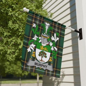 Peut inclure: Un drapeau à carreaux verts, noirs et dorés avec le nom "Murphy" affiché sur une bannière. Le drapeau présente un blason familial avec un arbre, un lion et un casque. Le drapeau est monté sur un poteau blanc fixé à un mur blanc.