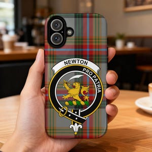 May include: A phone case featuring a gray, red, and blue plaid pattern. The case has a crest with the words "NEWTON PRO PATRIA" and a gold lion emblem. The phone case is held in a person's hand.