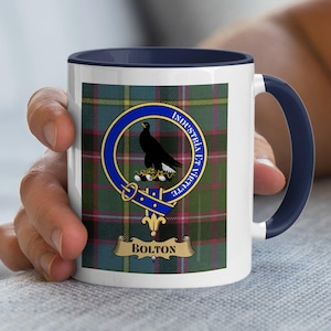Puede incluir: Taza de cerámica blanca con asa y borde azul marino. Presenta un colorido estampado de tartán y un escudo con un pájaro negro y la inscripción "Industria Et Virtute". El nombre "Bolton" se muestra en una pancarta.