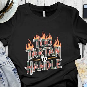 May include: Black t-shirt featuring the text "TOO TARTAN TO HANDLE" in a plaid design, surrounded by orange flames. The shirt is shown with a white hat, sunglasses, and a camera.