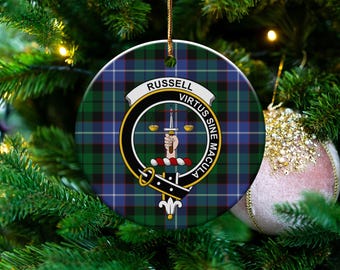 May include: Round Christmas ornament with a green, blue, and black plaid pattern. The ornament features a crest with the name "RUSSELL" and the motto "VIRTUS SINE MACULA". A gold string is attached for hanging. The ornament is displayed on a Christmas tree.