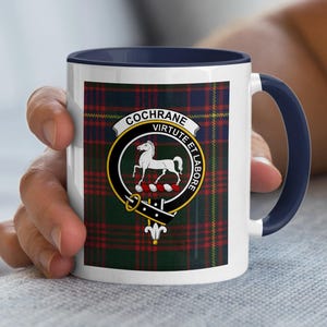 May include: White ceramic mug with a navy blue handle and rim. The mug features a tartan pattern with a crest that includes a white horse and the words "COCHRANE" and "VIRUTE ET LABORE".