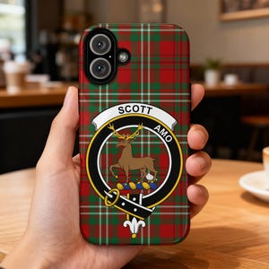 Puede incluir: Una funda de teléfono con un diseño de cuadros rojos, verdes y blancos. La funda presenta un escudo con un ciervo marrón, la palabra "SCOTT" y la palabra "AMO". La funda está diseñada para un teléfono inteligente.