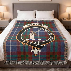 May include: A plaid throw blanket in shades of blue, green, and red, with a fringed edge. The blanket features a central emblem with the text "DALMAHOY" and "ABSQUE METU". The emblem includes a hand holding a sword.