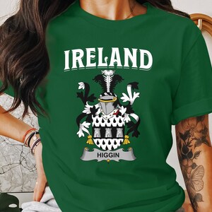 May include: A green t-shirt with the word "IRELAND" in white block letters above a detailed coat of arms. The coat of arms features a crest, shield, and banner with the name "HIGGIN".