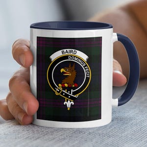 May include: White ceramic mug with a navy blue handle and rim. The mug features a tartan pattern with a crest that reads "BAIRD DOMINUS FECIT" and a brown eagle emblem.