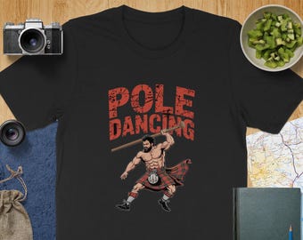 May include: Black t-shirt with a red graphic of a man in a kilt holding a pole with the text "POLE DANCING" above him.