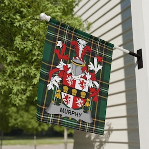 May include: A green, black, and yellow plaid flag with a family crest. The crest features a helmet, red and white accents, and the name "Murphy" on a banner. The flag is mounted on a white pole and black bracket.