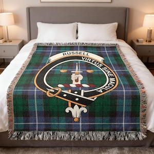 May include: A woven throw blanket with a green, blue, and black plaid pattern. The center features a crest with the name "RUSSELL" and the motto "VIRTUS SINE MACULA". The blanket has a fringed edge and is displayed on a bed.