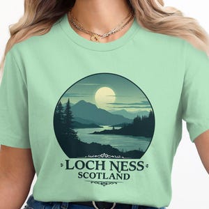 May include: A light green t-shirt with a graphic of a lake and mountains in a circle. The text "Loch Ness, Scotland" is printed below the graphic.