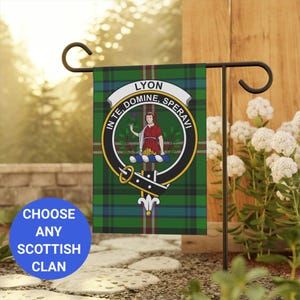 May include: A green, blue, and red Scottish clan flag with a crest featuring a woman holding a flower and the text "LYON IN TE DOMINE SPERAVI". The flag is attached to a black metal garden flag stand.