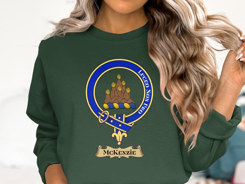McKenzie clan crest with motto "LUCEO NON TERO" on a dark green sweatshirt.