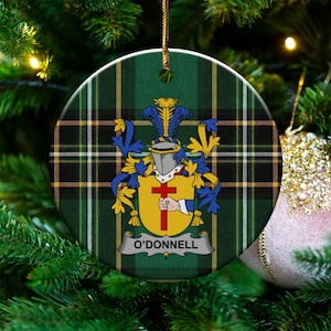 May include: A round ceramic ornament featuring a green, black, and yellow tartan plaid background. Centered is a heraldic crest with a silver helmet, blue and yellow mantling, and a yellow shield displaying a hand holding a red cross.