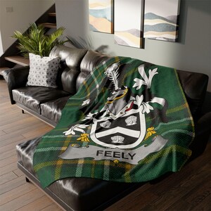 May include: A green, yellow, and black tartan throw blanket with a crest featuring a silver helmet, white shells, and the word "FEELY" in a banner.