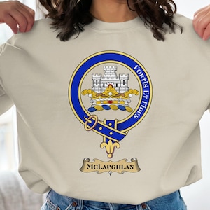 Könnte beinhalten: Beiges Sweatshirt mit einem blau-goldenen Wappen, das ein Schloss, den Schriftzug "Fortis et Fides" und den Namen "McLaughlin" zeigt. Das Wappen befindet sich mittig auf der Vorderseite des Sweatshirts.