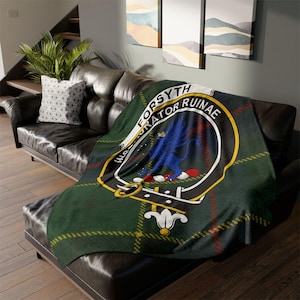 Op de afbeelding: Een groene tartan plaid met een wapen met een blauwe griffioen en de woorden "FORSYTH CRATOR RUINAE". De deken is gedrapeerd over een zwarte leren bank, met een patroon kussen.