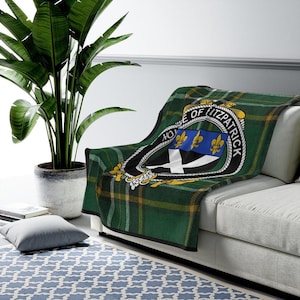 May include: Green, yellow, and black tartan throw blanket with a crest featuring a white cross and three blue fleurs-de-lis. The crest is surrounded by a gold circle with the text "House of Fitzpatrick".