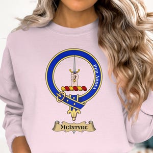 Light pink crewneck sweatshirt with McIntyre clan crest featuring a dagger and Latin motto.