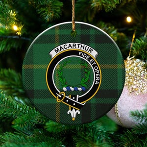 Op de afbeelding: Ronde kerstversiering met een groen en zwart geruit patroon. De versiering heeft een wapen met de woorden "Macarthur Fide et Opera". Het hangt aan een kerstboom met een roze bal.