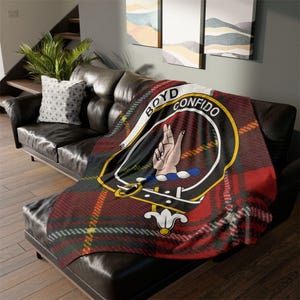 May include: A red, green and yellow tartan throw blanket with a black crest featuring a hand and the text "BOYD CONFIDO".