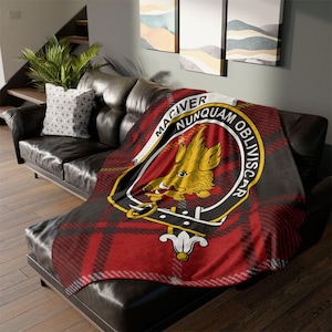 May include: A red, black and white tartan throw blanket with a crest featuring a yellow boar's head and the text "Maciver Nunquam Obliviscar".