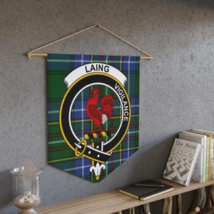 May include: A wall hanging featuring the Laing family crest. The crest includes a red rooster within a black and gold circular emblem, set against a green, blue, and yellow plaid background. The word "LAING" is displayed above the emblem, and "VIGILANCE" below.