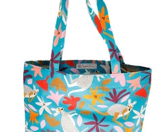 May include: A turquoise tote bag with a colorful pattern of kangaroos and flowers. The bag has two handles and a spacious interior. The design includes orange, pink, and white floral elements, creating a vibrant and playful aesthetic.