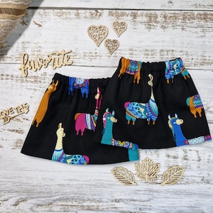 Puede incluir: Tela negra con un colorido estampado de llamas. Las llamas son de varios colores, incluyendo azul, rosa y naranja, con diseños geométricos. La tela está fruncida en la parte superior, sugiriendo una falda o prenda similar.