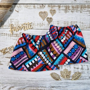 Puede incluir: Un par de shorts estampados coloridos con cintura elástica. Los shorts presentan un diseño geométrico en tonos rojos, azules, morados y marrones. Recortes de madera con forma de corazón y hoja están dispersos.