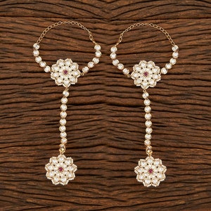 May include: A pair of gold-tone hand chains with white and red gemstone embellishments. Each chain features a floral design with a central red gemstone.