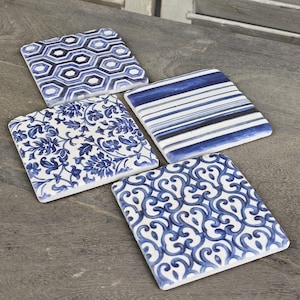 May include: Four square ceramic coasters with blue and white patterns. Designs include a floral pattern, stripes, a geometric hexagon pattern, and a swirling pattern. The coasters are arranged on a wooden surface.