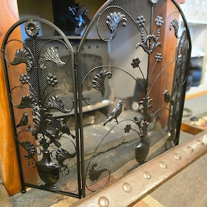 May include: Black metal fireplace screen with a decorative floral design and bird accents. The screen is made of mesh and has three panels.