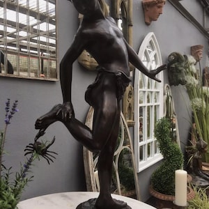 May include: Bronze sculpture of a young person playfully interacting with a crab. The figure is in a dynamic pose, with one leg raised and the other extended. The sculpture is set on a round base.
