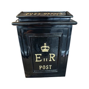 Może przedstawiać: Czarny, prostokątny pojemnik na listy ze złotymi literami. Na górze napis "POST OFFICE". Na froncie złota korona nad napisami "E II R" i "POST". Skrzynka ma błyszczącą powierzchnię.