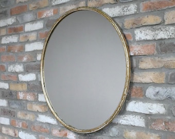 Peut inclure: Miroir ovale avec un cadre doré texturé. Le miroir est monté sur un mur de briques avec un mélange de briques rouges, blanches et grises. Le cadre présente un motif décoratif et organique.