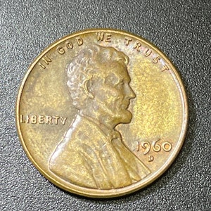 May include: A copper-colored US penny with the words "IN GOD WE TRUST" and "LIBERTY" around the edge. The year "1960" is printed on the coin with a "D" mint mark.