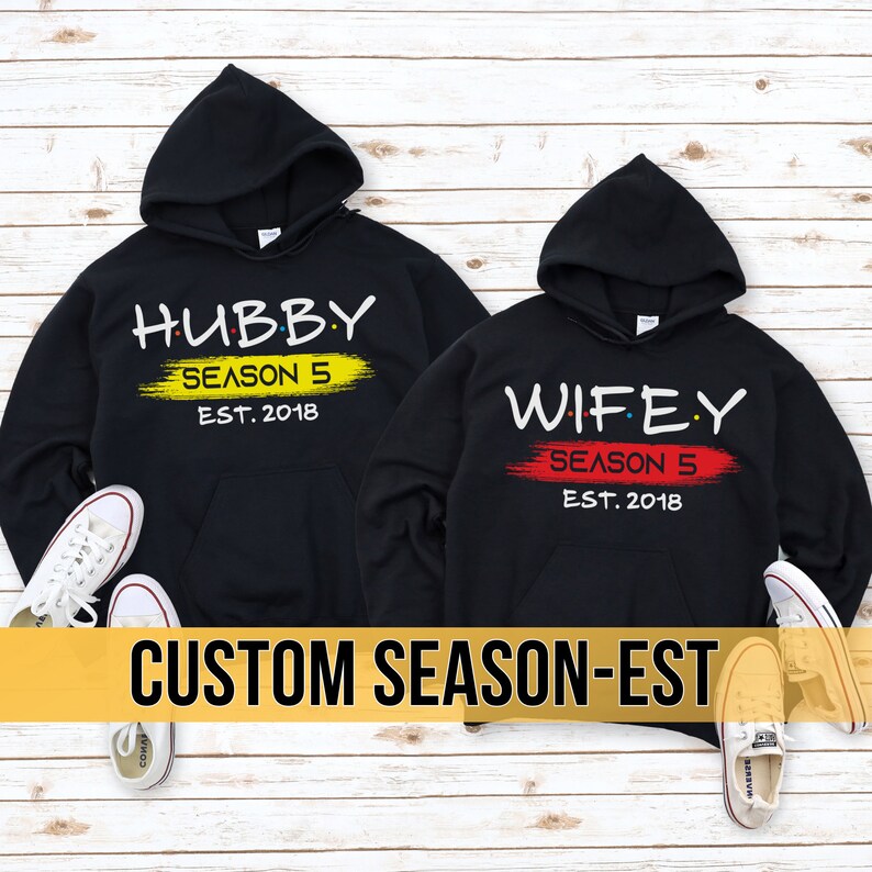 May include: Two black hoodies with white text and a red and yellow paint stroke. The text on the hoodies reads "Hubby Season 5 Est. 2018" and "Wifey Season 5 Est. 2018".