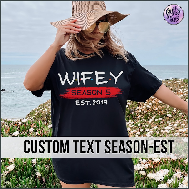 May include: Black t-shirt with the text "WIFEY SEASON 5 EST. 2019" in white and red. The text is stylized to look like the Friends logo.