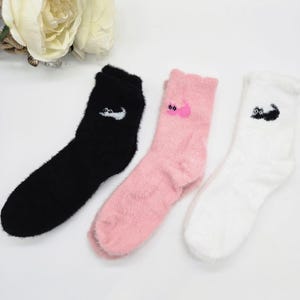 May include: Three pairs of fuzzy socks with different animal designs. One pair is black with a white animal, one pair is pink with a pink animal, and one pair is white with a black animal.