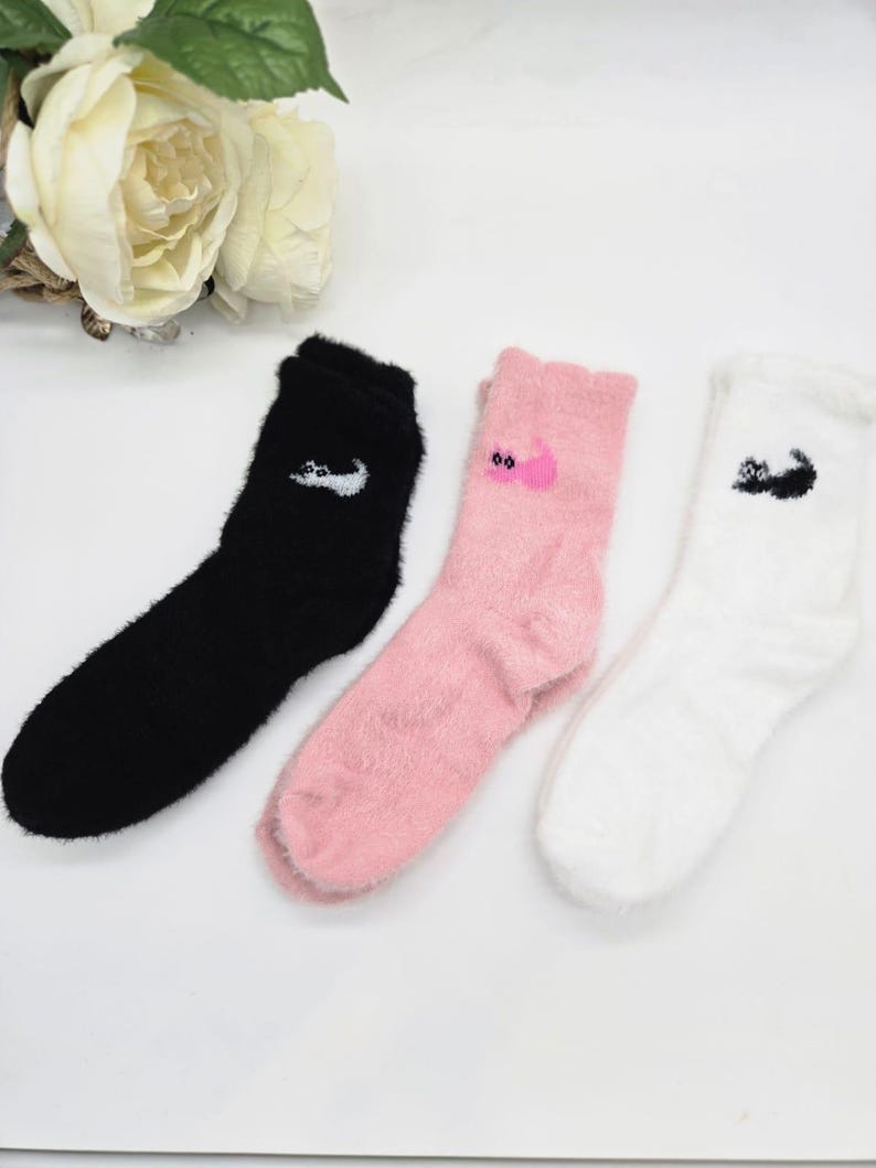 May include: Three pairs of fuzzy socks with different animal designs. One pair is black with a white animal, one pair is pink with a pink animal, and one pair is white with a black animal.