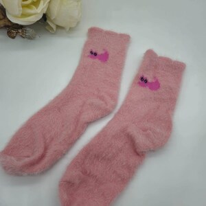 May include: A pair of pink fuzzy socks with a pink cat design on each sock.