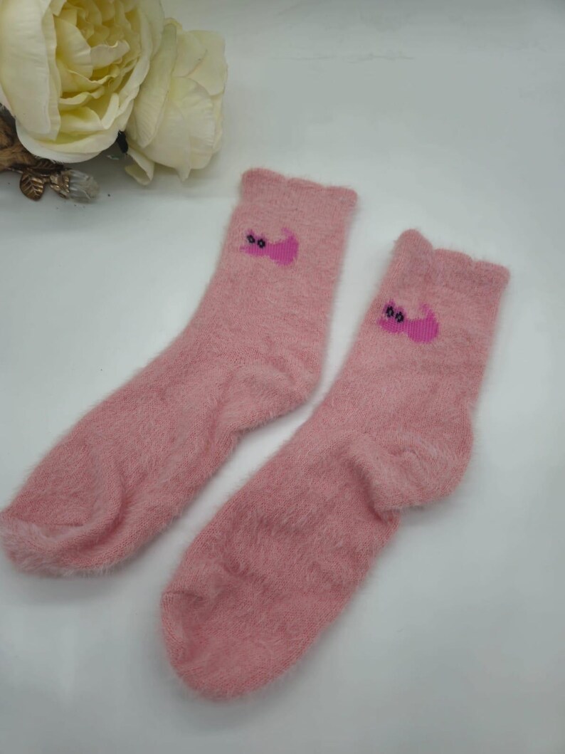May include: A pair of pink fuzzy socks with a pink cat design on each sock.