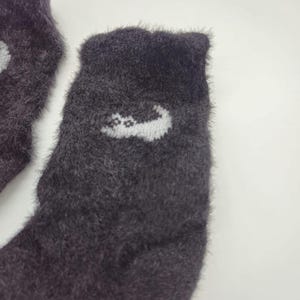 May include: A pair of fuzzy dark gray socks with a white cat design on one sock.