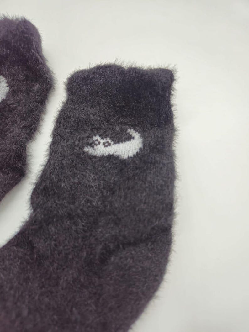 May include: A pair of fuzzy dark gray socks with a white cat design on one sock.