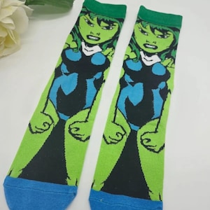 May include: A pair of green and blue socks with a cartoon image of a female superhero. The socks have a blue cuff at the bottom.