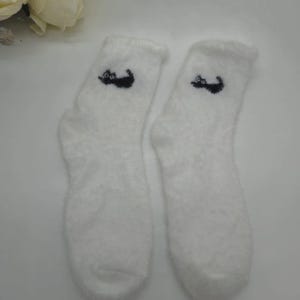 May include: A pair of white fuzzy socks with a black cat design on each sock.