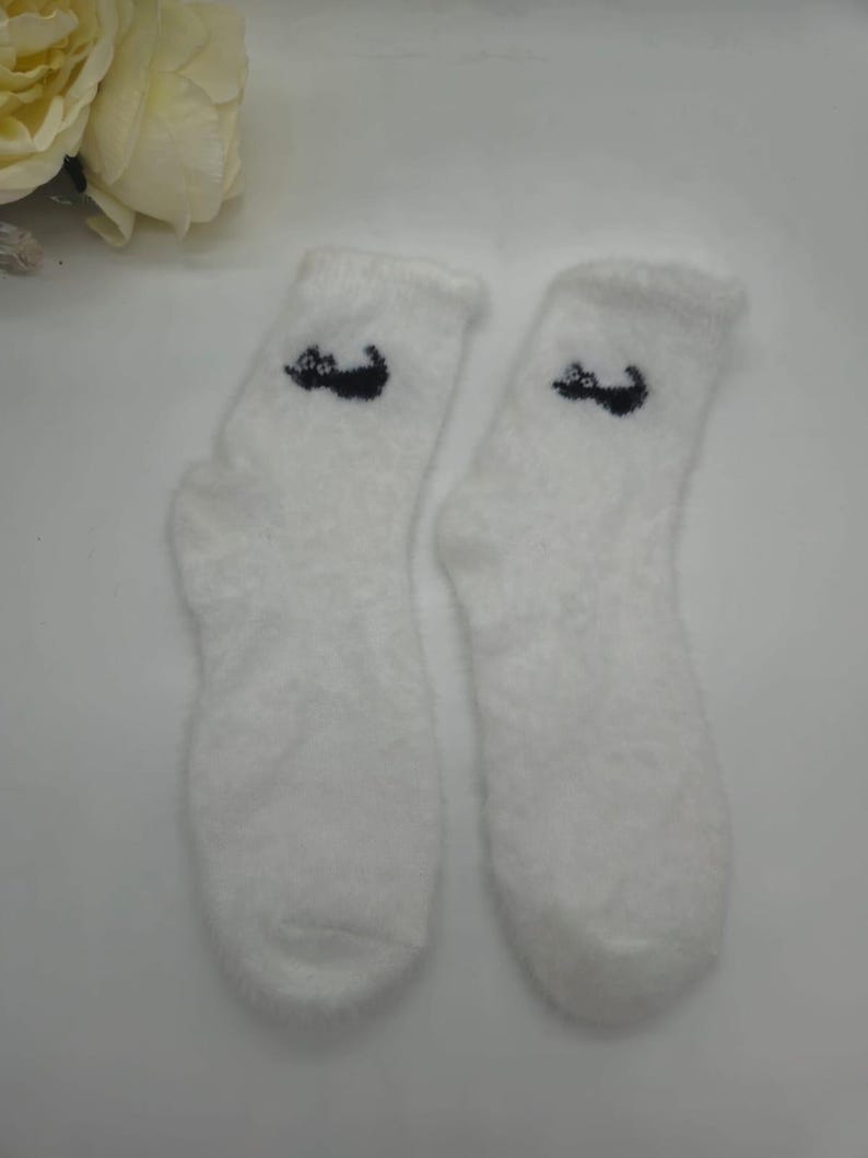 May include: A pair of white fuzzy socks with a black cat design on each sock.