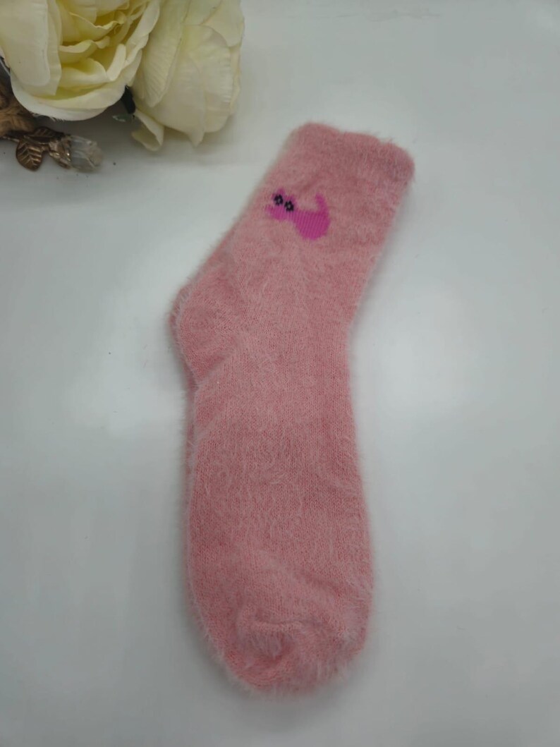 May include: A pair of pink fuzzy socks with a pink cat design. The cat has pink ears and a pink tail.