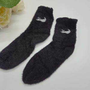 May include: A pair of black fuzzy socks with a white cat design on each sock.