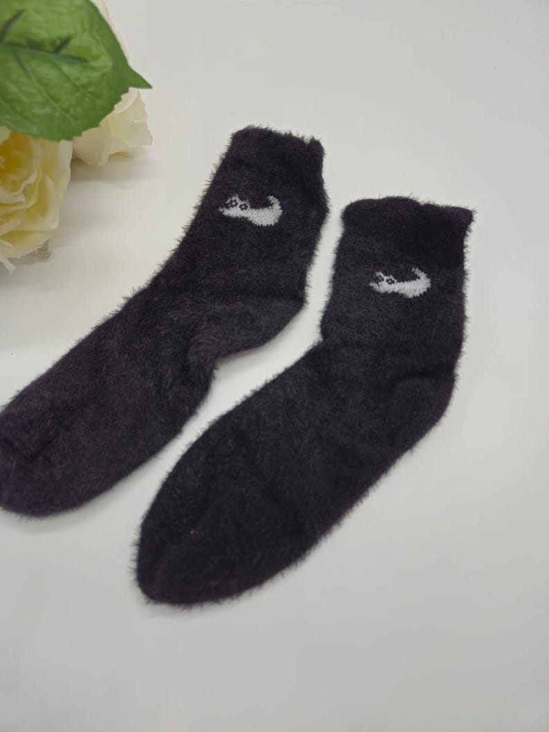 May include: A pair of black fuzzy socks with a white cat design on each sock.